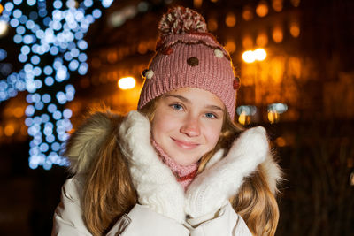 Portrait of young woman standing against illuminated christmas tree