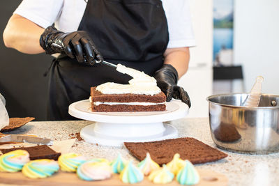Pastry chef cook confectioner or baker in black gloves and black kitchen apron makes a cake