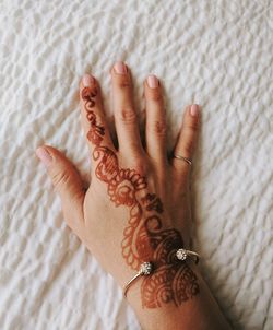 Cropped hand of woman with henna tattoo on bed