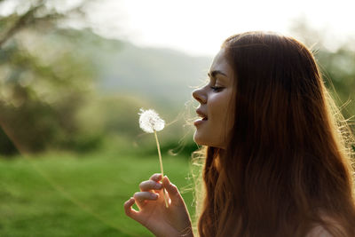 Side view of young woman blowing bubbles while standing outdoors