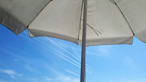 Low angle view of parasol against vapor trails in sky
