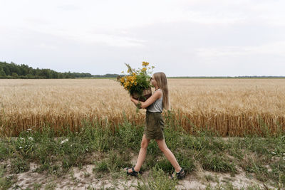 Girl holding tansy flower basket while walking by wheat field