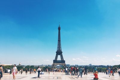 People around eiffel tower in city against blue sky