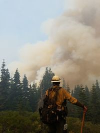 Rear view of firefighter standing in forest against smoke