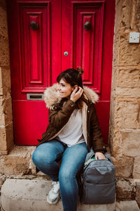 Full length of woman with backpack sitting by door