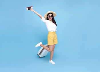 Woman holding umbrella while standing against blue background