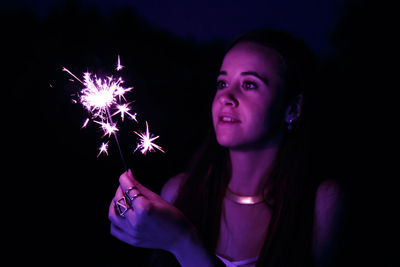 Close-up of woman holding sparkler at night