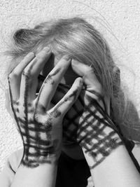 Close-up of girl covering face with hands against wall