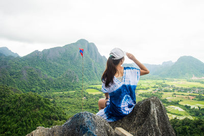 Rear view of woman sitting on rock against sky