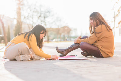 Females writing on posters sitting on street