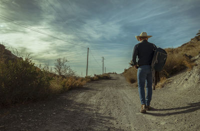 Rear view of adult man in cowboy hat walking on dirt road