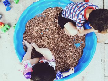 Directly above shot of siblings playing in wading pool with beans