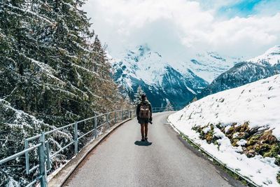 Rear view of man walking on road against snowcapped mountains