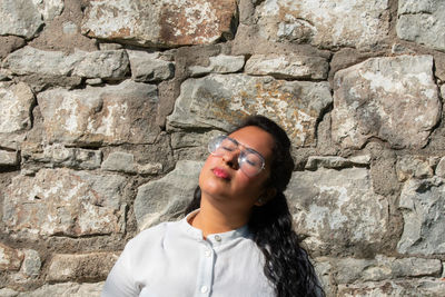 Portrait of young woman standing against stone wall