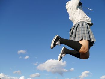 Low angle view of woman jumping against blue sky