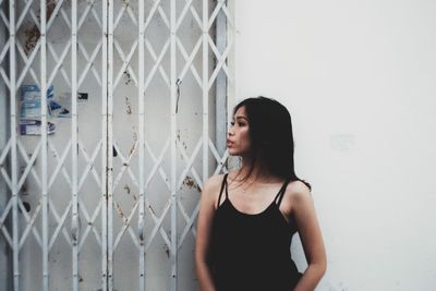 Woman looking away while standing against wall