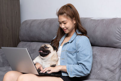 Smiling woman with dog using laptop at home