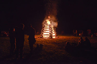 Silhouette people enjoying bonfire on field at night