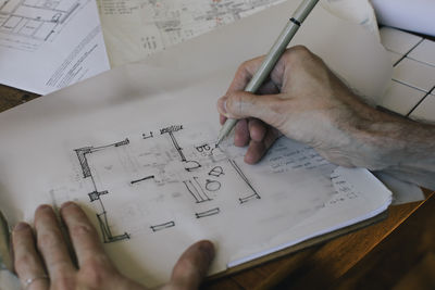 Cropped hands of male architect sketching blueprint on paper at desk in home office