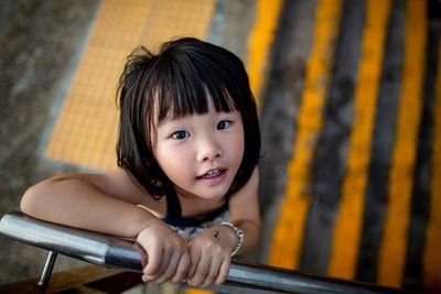 Portrait of smiling baby girl standing by railing 