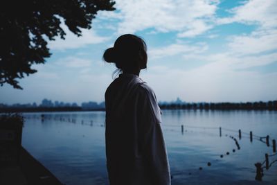 Rear view of silhouette woman standing by lake against sky