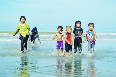 Playful children running in sea against sky