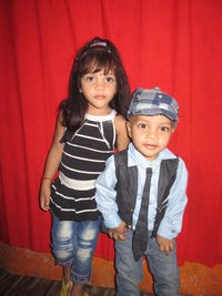 Portrait of siblings standing against curtain