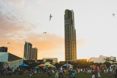 Crowd in city against sky during sunset