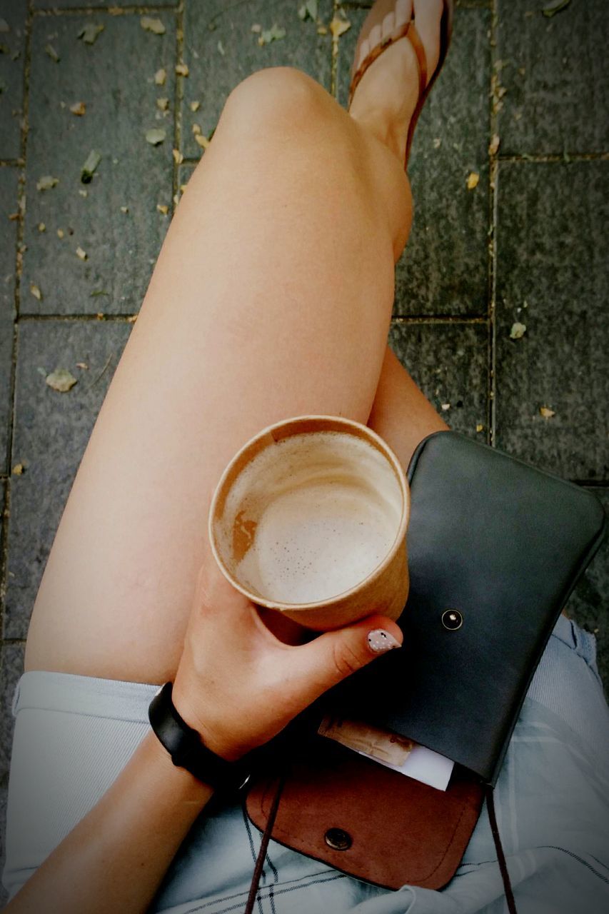 LOW SECTION OF WOMAN HOLDING COFFEE CUP AGAINST WHITE WALL