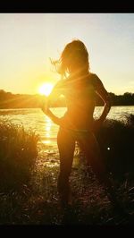 Rear view of silhouette woman standing by lake at sunset