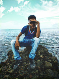 Side view of man sitting on rock at beach against sky