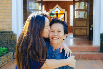 Portrait of mother being kissed by daughter while standing outdoors