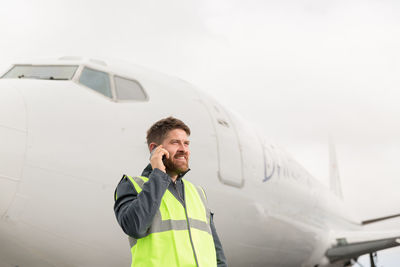 Male technician speaking on smartphone near plane