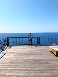 Man on pier by sea against clear blue sky