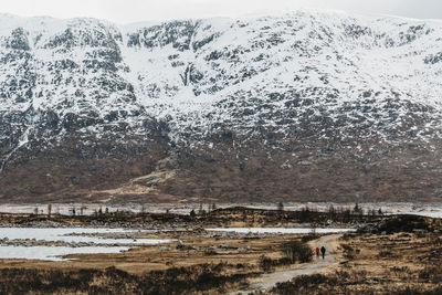 Rear view of couple walking on landscape against snowcapped mountain