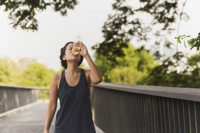 Woman drinking energy drink after jogging in the park.