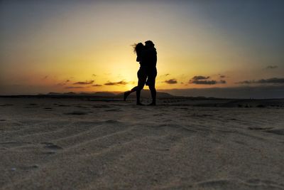 Silhouette couple standing on beach against sky during sunset