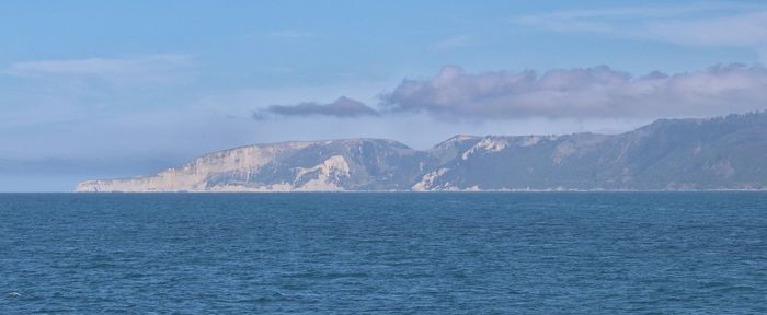 Scenic view of sea by mountain against sky