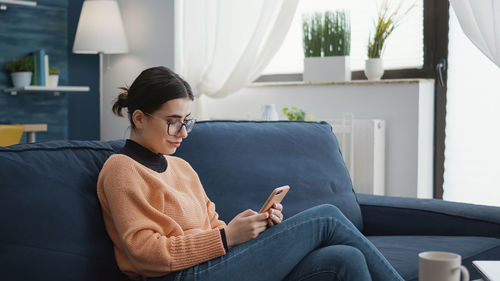 Smiling woman using mobile phone while sitting on sofa at home