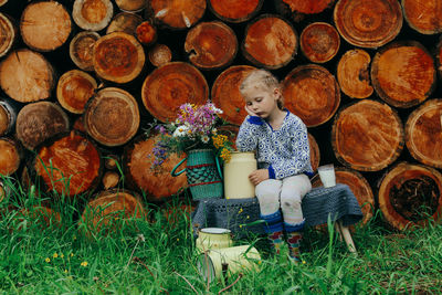 Rustic style, a girl in casual clothes sits on a bench against the background of a woodpile