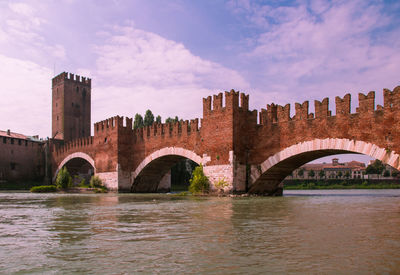 Arch bridge over river by buildings against sky