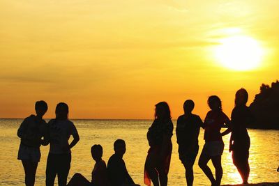 Silhouette people standing on beach against orange sky