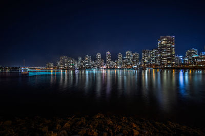 Illuminated city by sea against sky at night