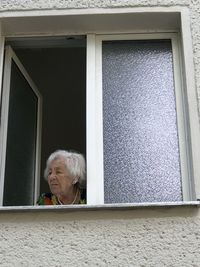 Portrait of woman looking through window in building