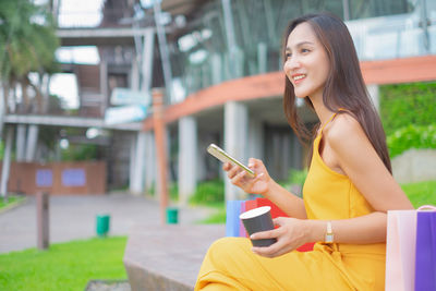 Smiling young woman using mobile phone while sitting on laptop