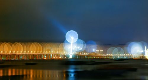 Defocused lights of bridge over lake against sky at night