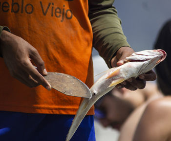 Midsection of man holding fish and knife
