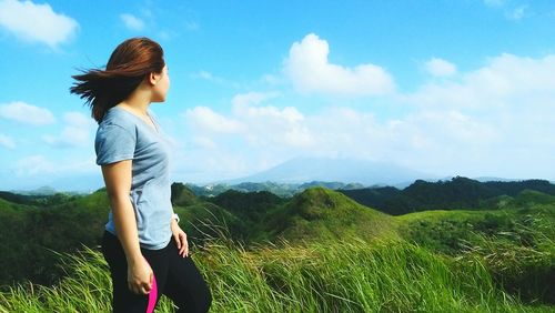 Side view of woman standing on grassy field against sky