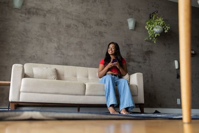 Young black woman working at home with smartphone sitting on her couch . home office