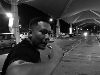 Close-up portrait of man smoking electronic cigarette at illuminated street